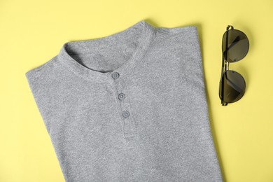Photo of Grey t-shirt and sunglasses on yellow background, flat lay. Mockup for design