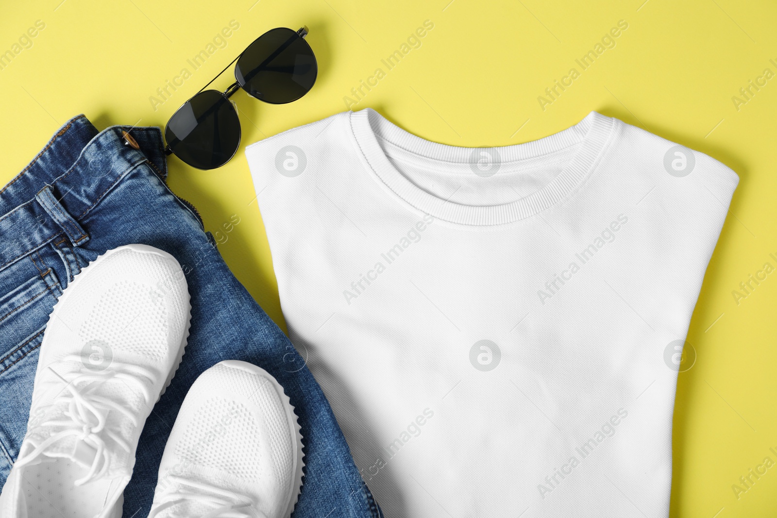 Photo of White t-shirt, jeans, sunglasses and sneakers on yellow background, flat lay. Mockup for design