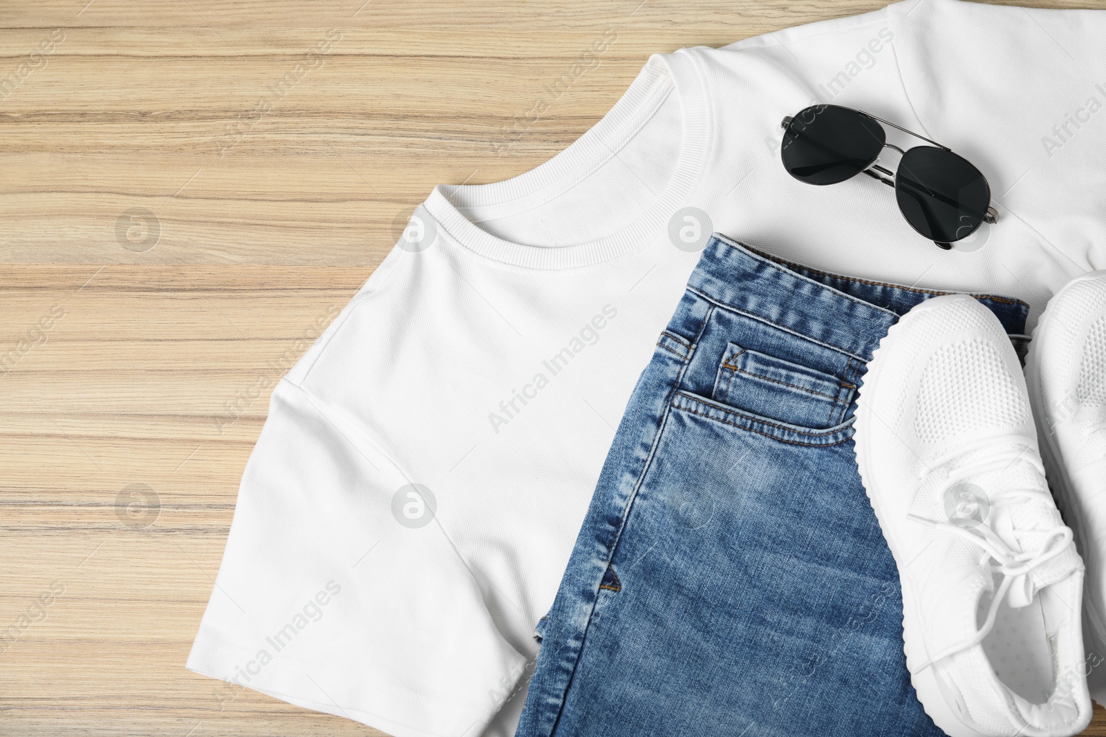 Photo of White t-shirt, jeans, sunglasses and sneakers on wooden table, flat lay. Mockup for design