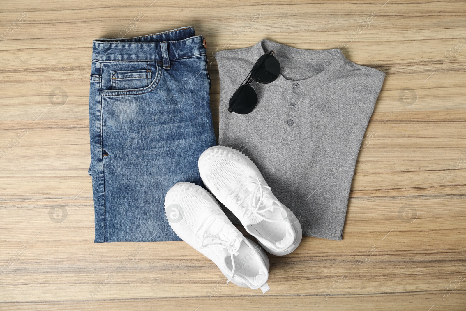 Photo of Grey t-shirt, jeans, sunglasses and sneakers on wooden table, flat lay. Mockup for design