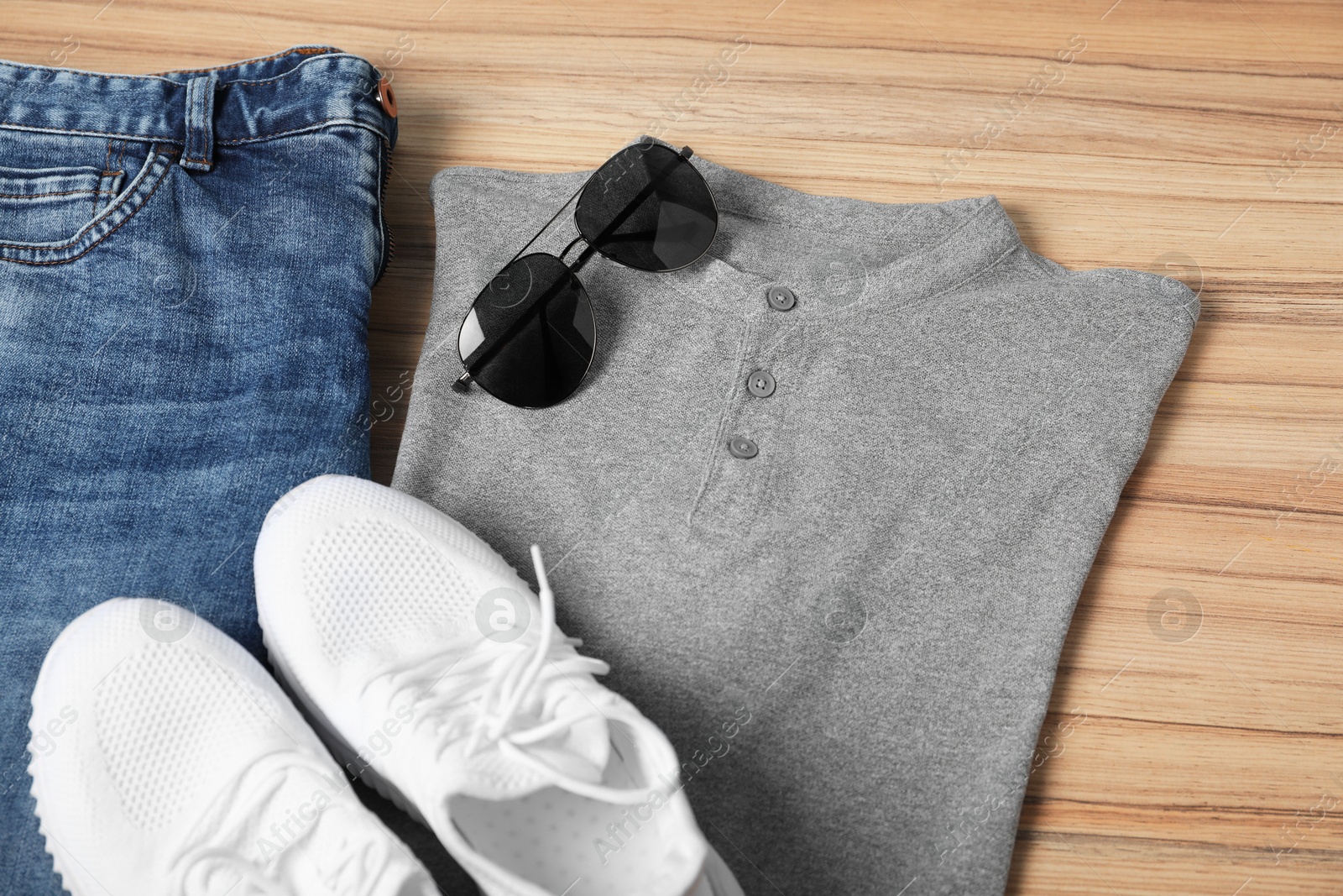 Photo of Grey t-shirt, jeans, sunglasses and sneakers on wooden table, above view. Mockup for design