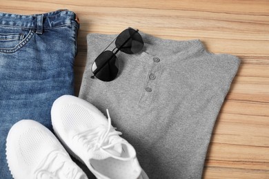 Photo of Grey t-shirt, jeans, sunglasses and sneakers on wooden table, above view. Mockup for design