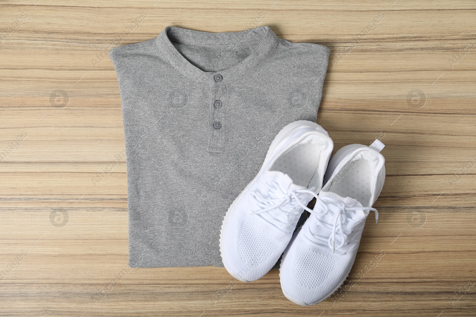 Photo of Grey t-shirt and sneakers on wooden table, top view. Mockup for design