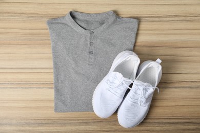 Photo of Grey t-shirt and sneakers on wooden table, top view. Mockup for design