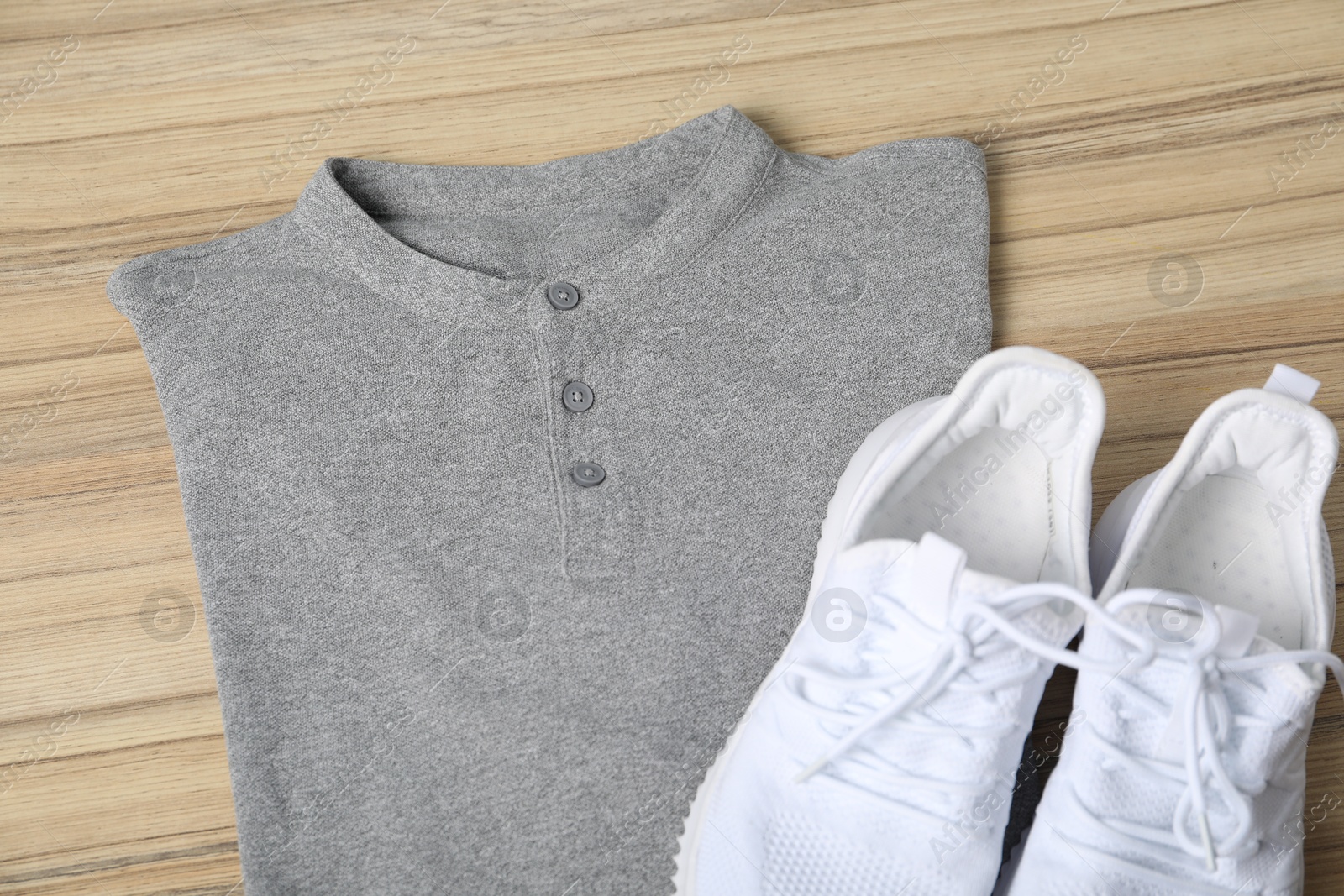 Photo of Grey t-shirt and sneakers on wooden table, top view. Mockup for design