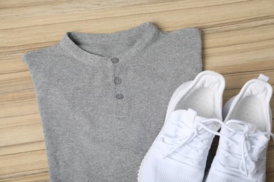 Photo of Grey t-shirt and sneakers on wooden table, top view. Mockup for design