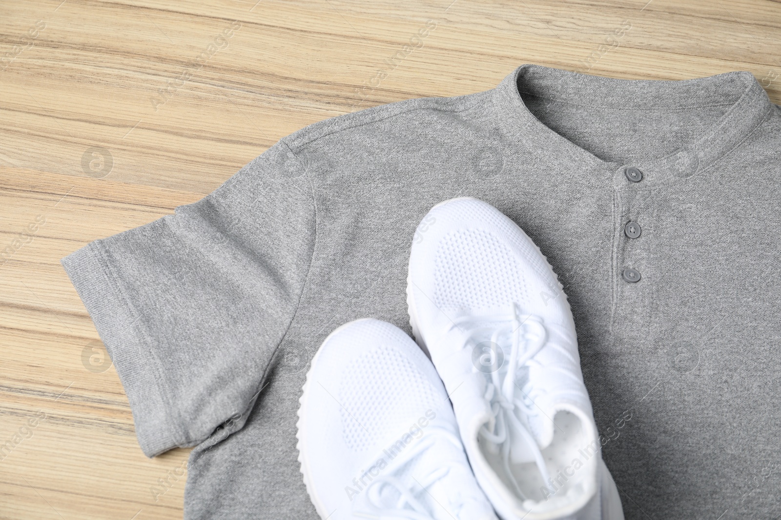 Photo of Grey t-shirt and sneakers on wooden table, top view. Mockup for design