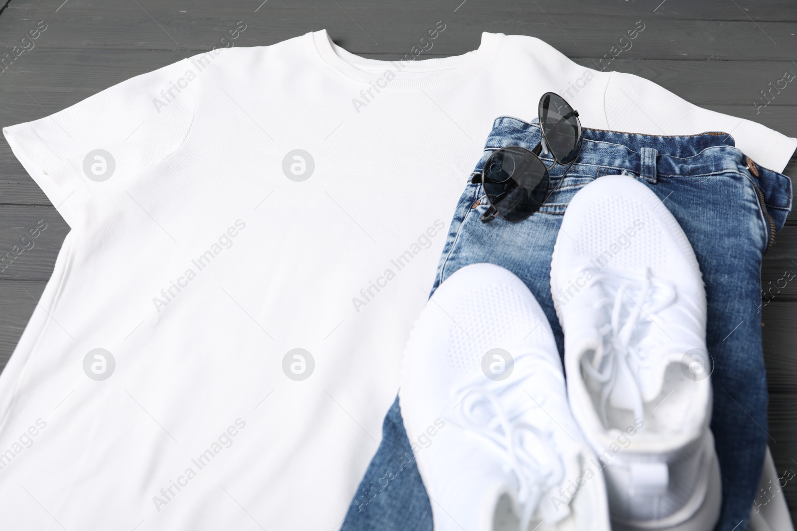 Photo of White t-shirt, jeans, sunglasses and sneakers on grey wooden table, closeup. Mockup for design