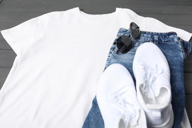 Photo of White t-shirt, jeans, sunglasses and sneakers on grey wooden table, closeup. Mockup for design