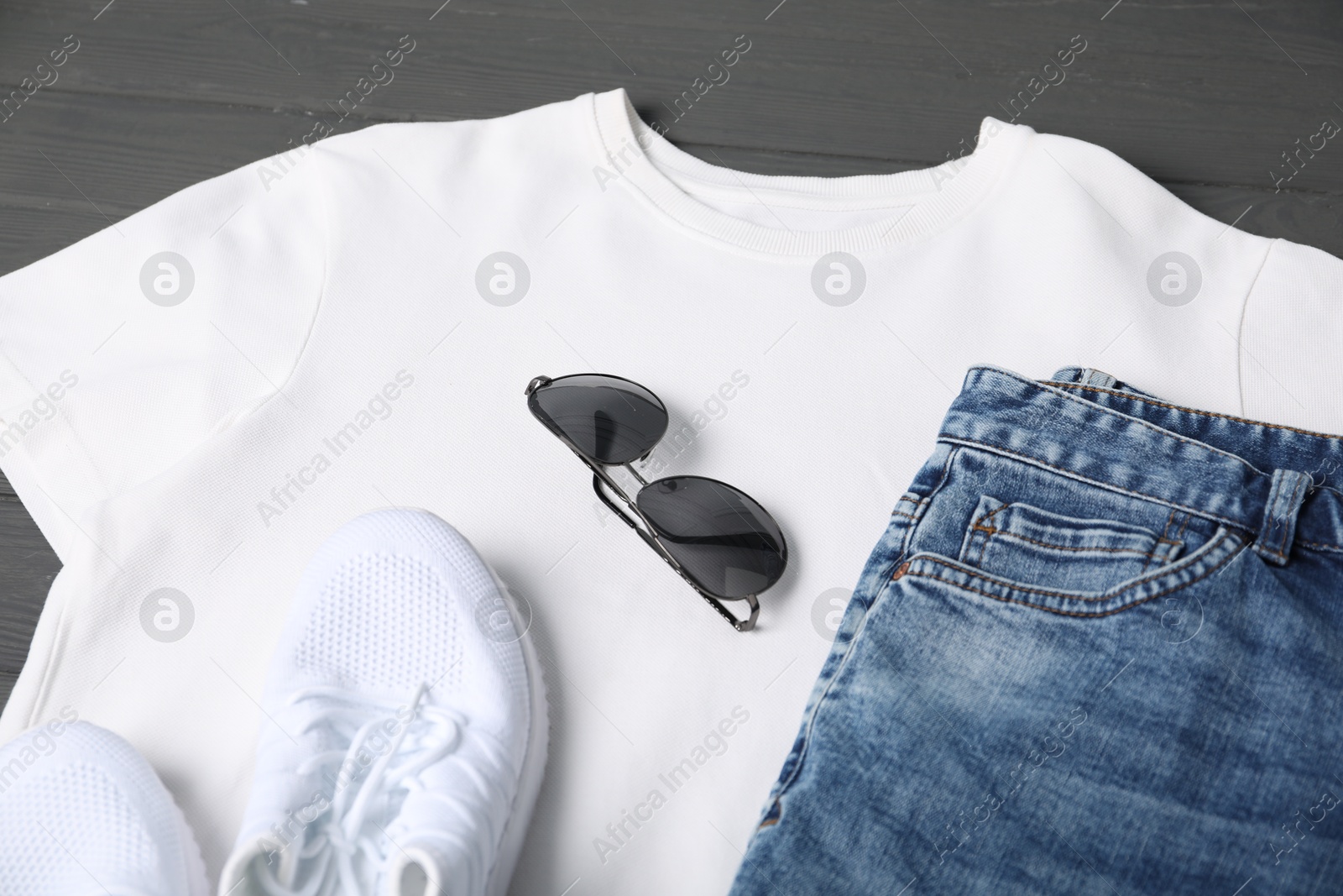 Photo of White t-shirt, jeans, sunglasses and sneakers on grey wooden table, closeup. Mockup for design