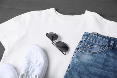 Photo of White t-shirt, jeans, sunglasses and sneakers on grey wooden table, closeup. Mockup for design