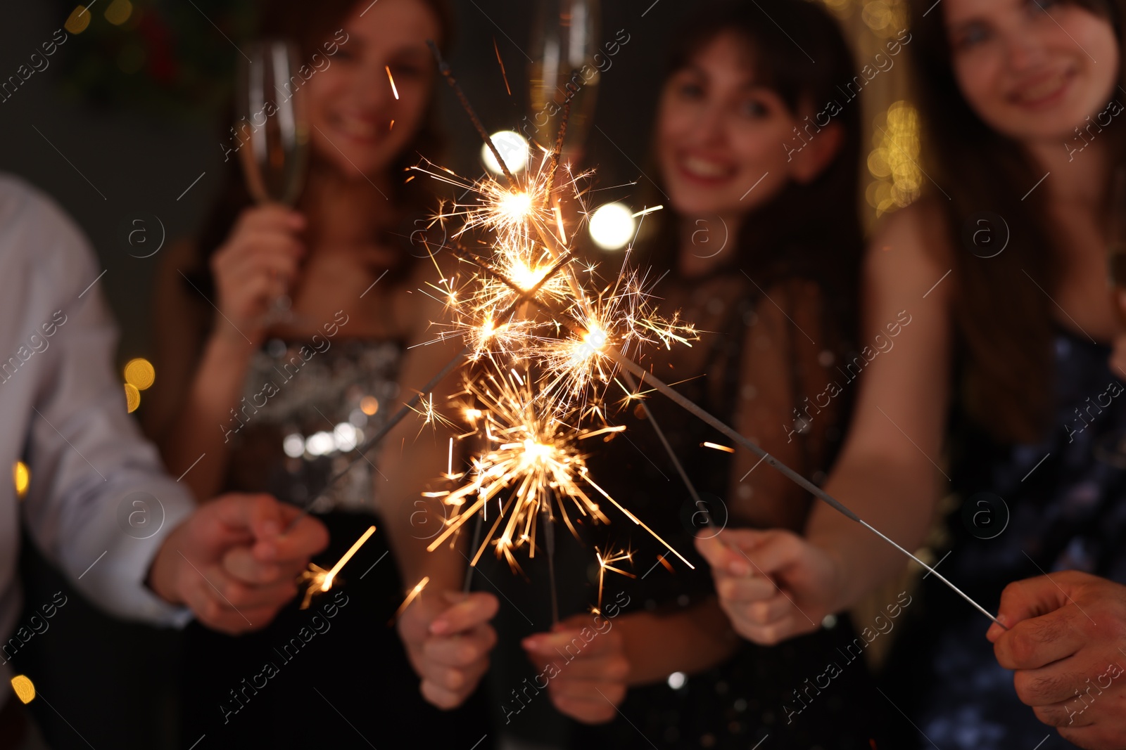 Photo of Friends celebrating New Year with sparklers and wine glasses indoors, selective focus