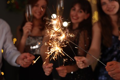 Photo of Friends celebrating New Year with sparklers and wine glasses indoors, selective focus