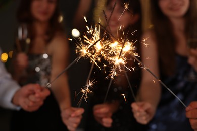 Photo of Friends celebrating New Year with sparklers and wine glasses indoors, selective focus