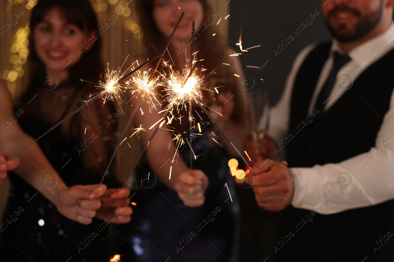 Photo of Friends celebrating New Year with sparklers and wine glasses indoors, selective focus