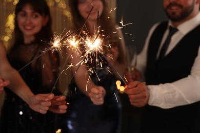 Photo of Friends celebrating New Year with sparklers and wine glasses indoors, selective focus