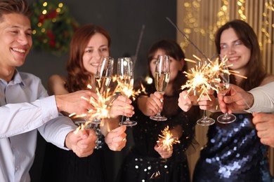 Photo of Friends celebrating New Year with sparklers and wine glasses indoors, selective focus