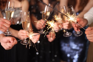 Photo of Friends celebrating New Year with sparklers and wine glasses indoors, closeup
