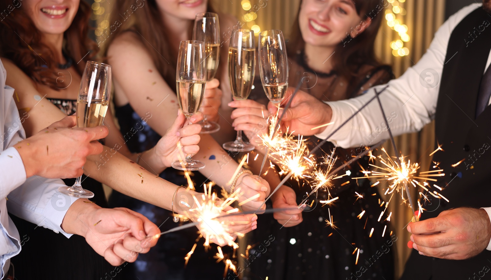 Photo of Friends celebrating New Year with sparklers and wine glasses indoors, selective focus