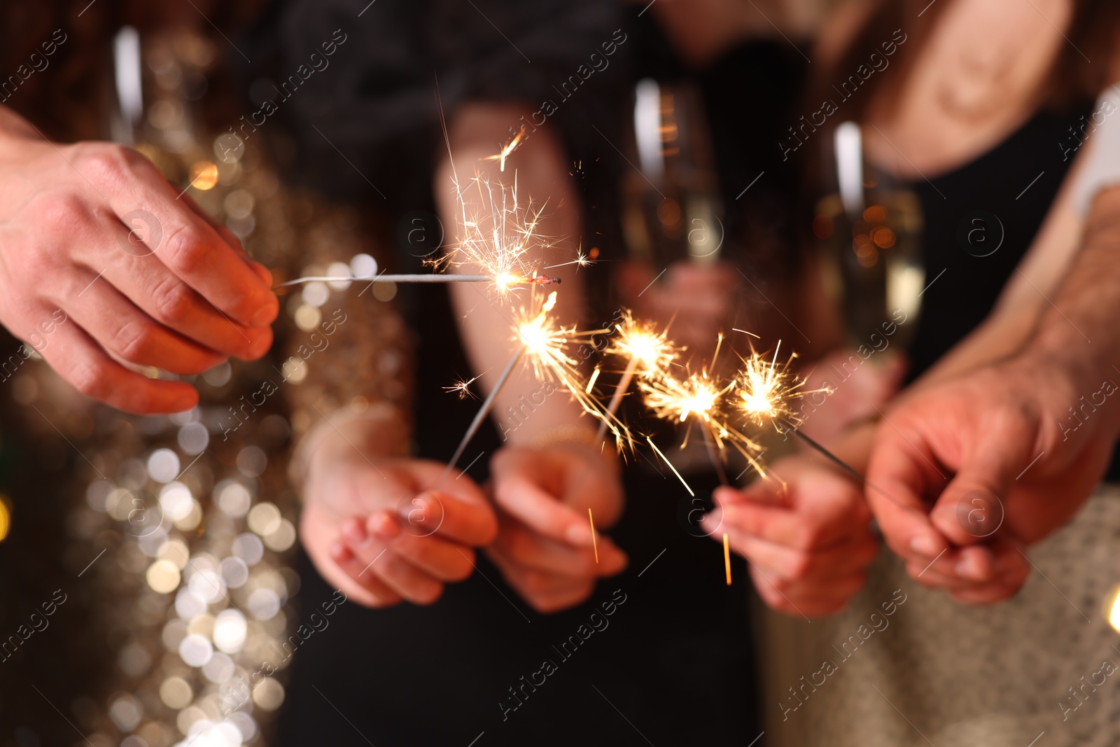 Photo of Friends celebrating New Year with sparklers and wine glasses indoors, closeup