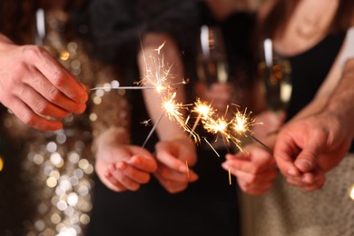 Photo of Friends celebrating New Year with sparklers and wine glasses indoors, closeup