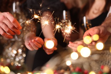 Photo of Friends celebrating New Year with sparklers and wine glasses indoors, closeup