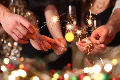 Photo of Friends celebrating New Year with sparklers and wine glasses indoors, closeup