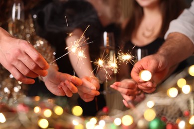 Photo of Friends celebrating New Year with sparklers and wine glasses indoors, closeup