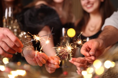Photo of Friends celebrating New Year with sparklers and wine glasses indoors, closeup