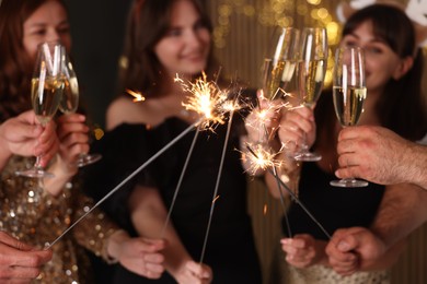 Photo of Friends celebrating New Year with sparklers and wine glasses indoors, selective focus