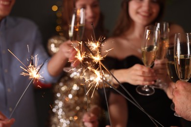 Photo of Friends celebrating New Year with sparklers and wine glasses indoors, selective focus