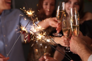 Photo of Friends celebrating New Year with sparklers and wine glasses indoors, selective focus