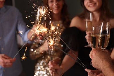 Photo of Friends celebrating New Year with sparklers and wine glasses indoors, selective focus