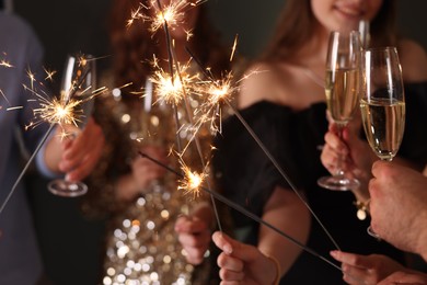 Photo of Friends celebrating New Year with sparklers and wine glasses indoors, closeup