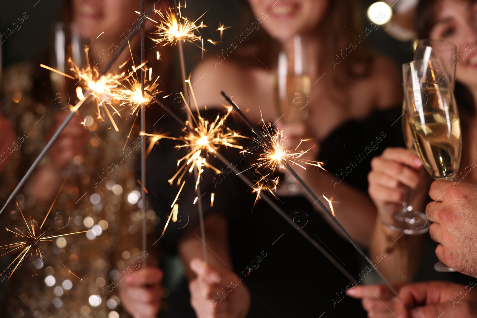 Photo of Friends celebrating New Year with sparklers and wine glasses indoors, closeup