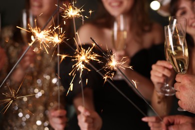 Photo of Friends celebrating New Year with sparklers and wine glasses indoors, closeup