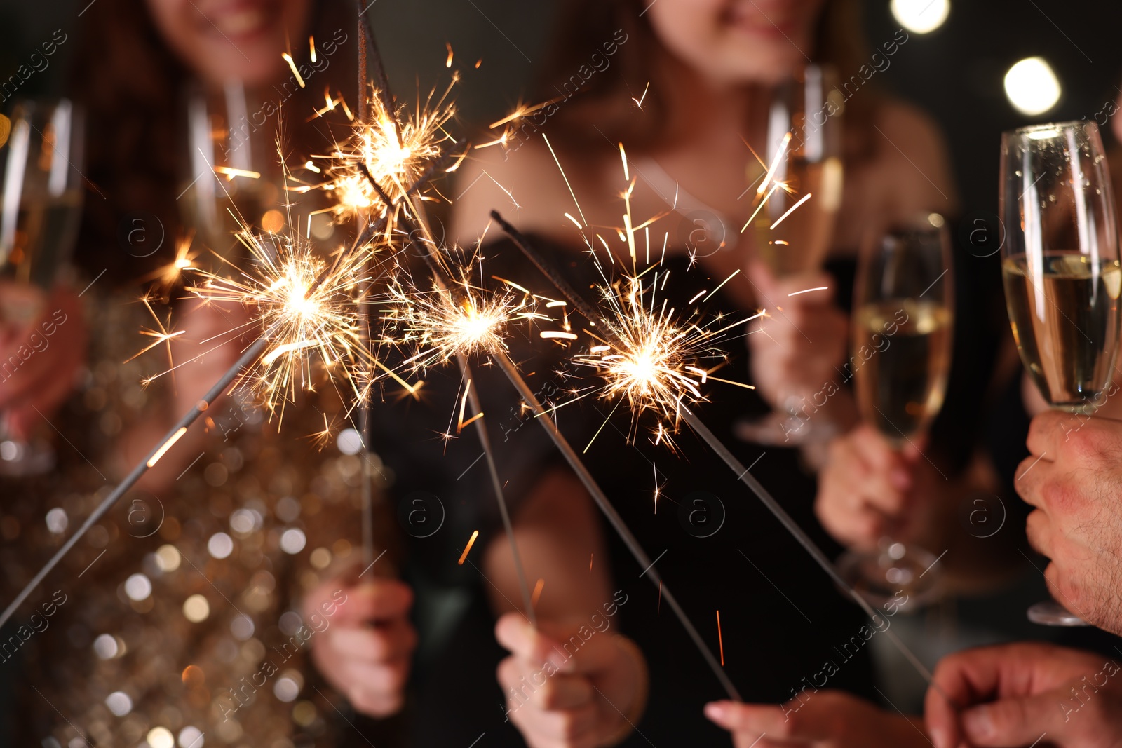 Photo of Friends celebrating New Year with sparklers and wine glasses indoors, closeup