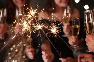 Photo of Friends celebrating New Year with sparklers and wine glasses indoors, closeup
