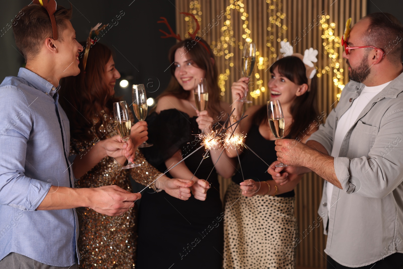 Photo of Friends celebrating New Year with sparklers and wine glasses indoors
