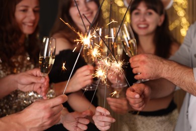 Photo of Friends celebrating New Year with sparklers and wine glasses indoors, selective focus