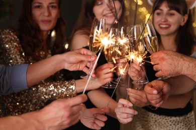 Photo of Friends celebrating New Year with sparklers and wine glasses indoors, selective focus