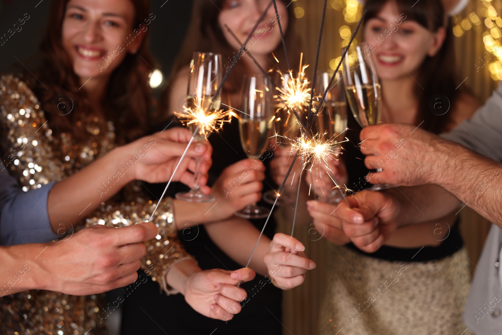 Photo of Friends celebrating New Year with sparklers and wine glasses indoors, selective focus