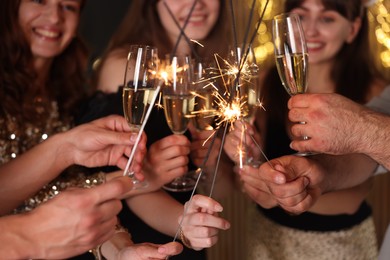 Photo of Friends celebrating New Year with sparklers and wine glasses indoors, selective focus