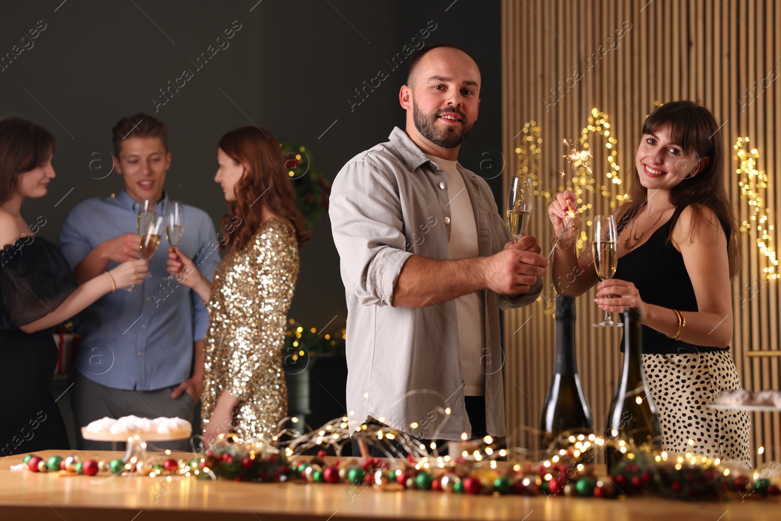 Photo of Friends celebrating New Year with sparklers and wine glasses indoors