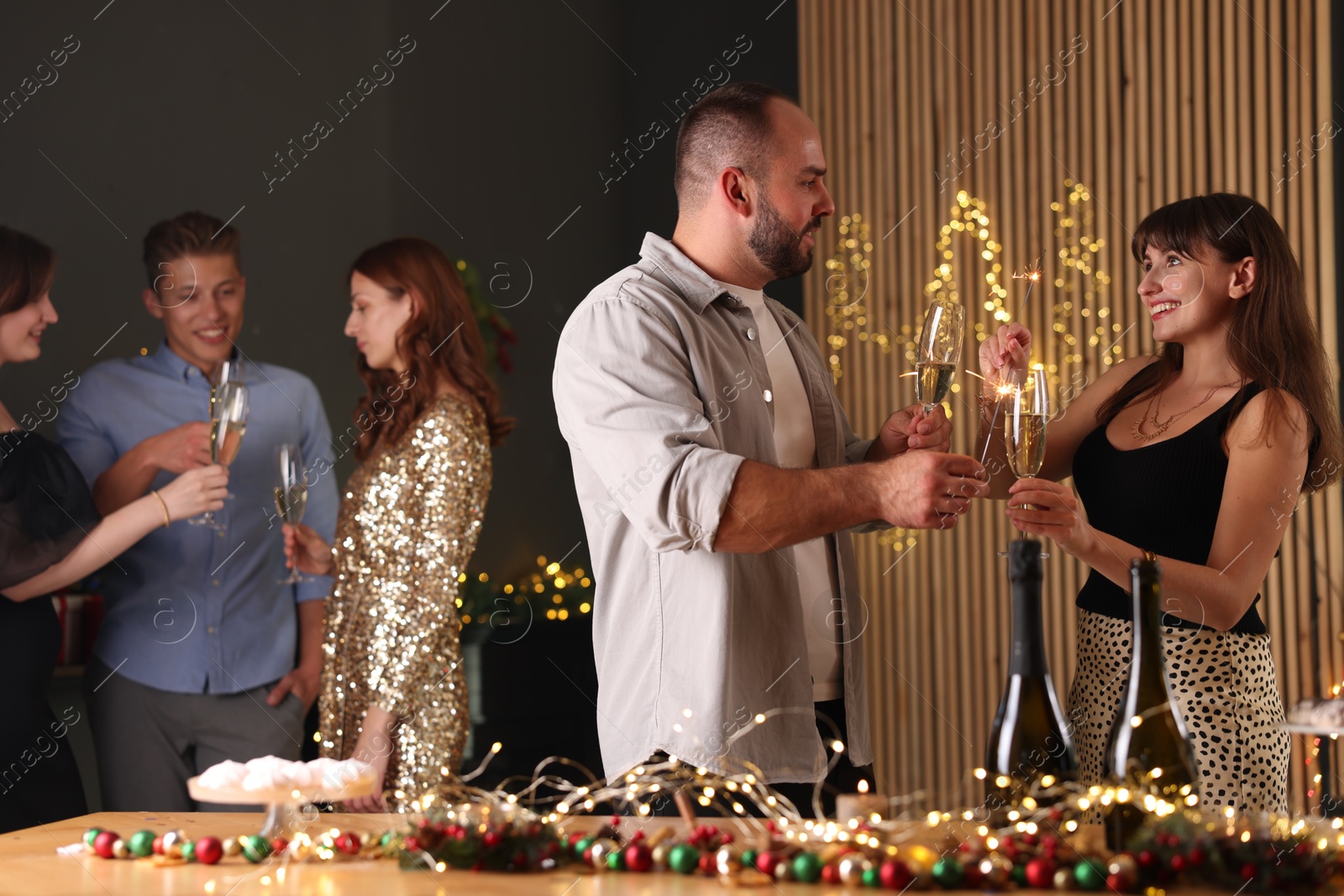 Photo of Friends celebrating New Year with sparklers and wine glasses indoors