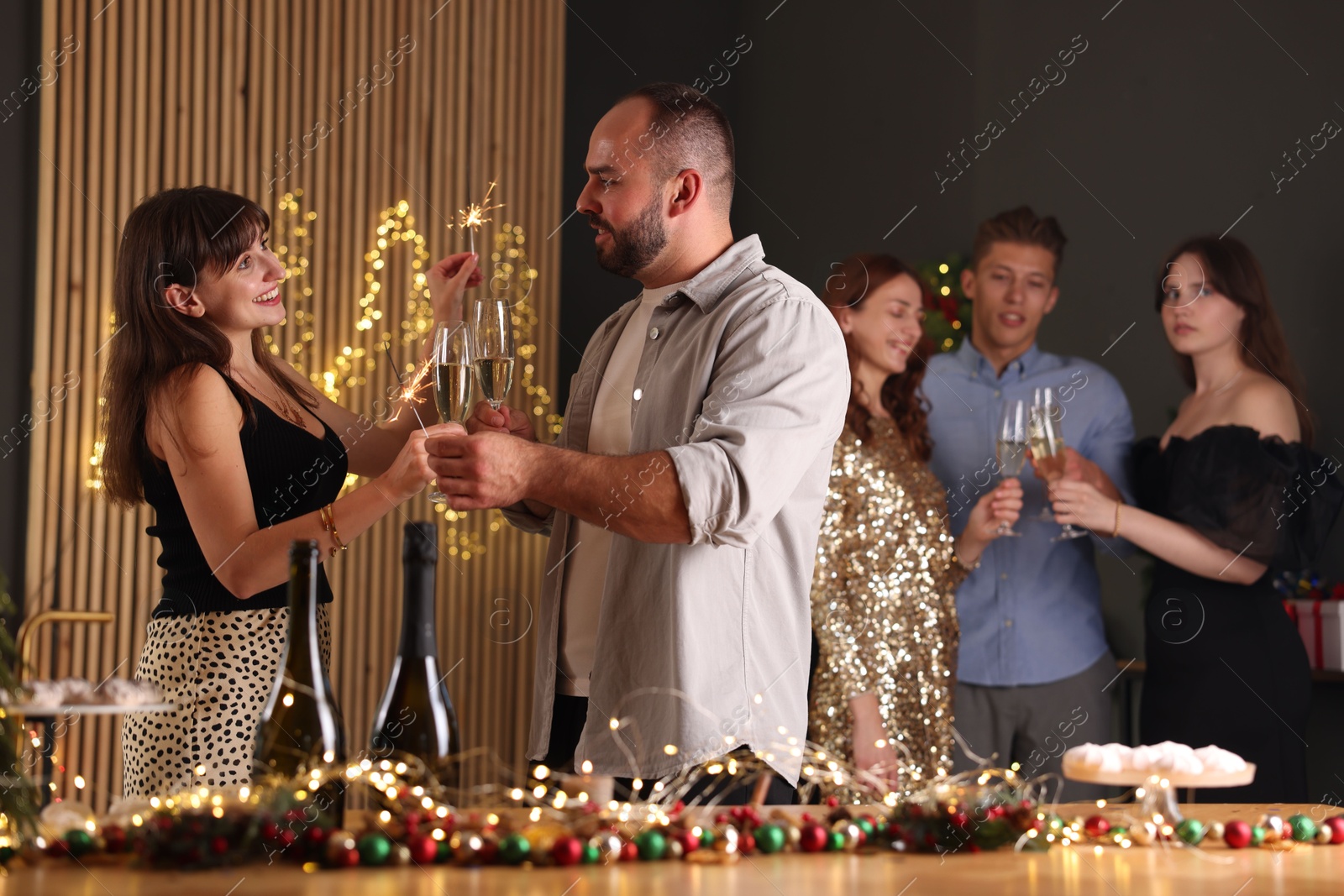 Photo of Friends celebrating New Year with sparklers and wine glasses indoors
