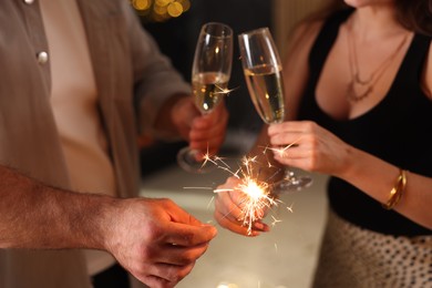 Photo of Friends celebrating New Year with sparklers and wine glasses indoors, closeup