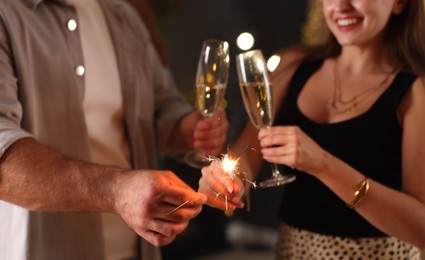 Photo of Friends celebrating New Year with sparklers and wine glasses indoors, closeup