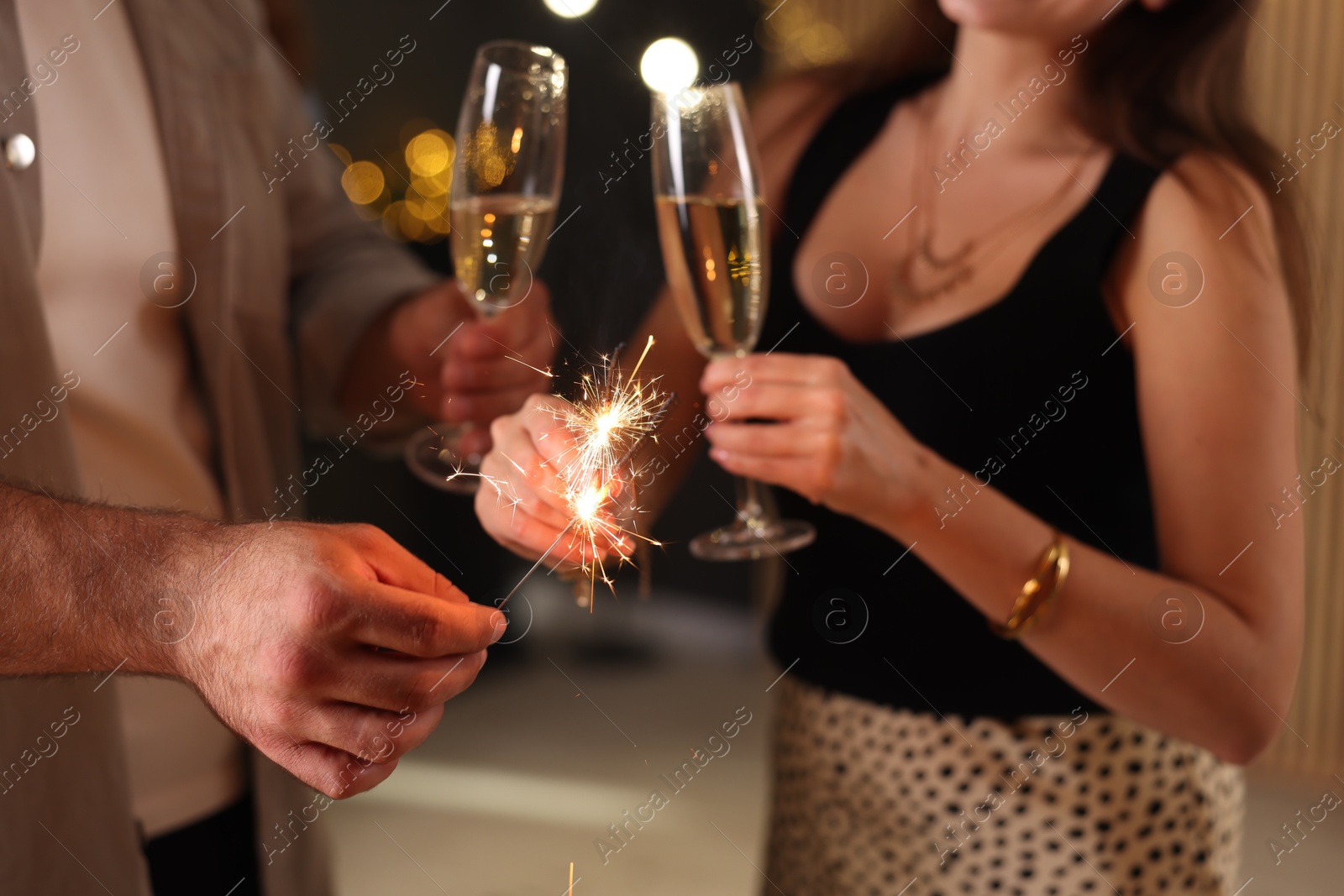 Photo of Friends celebrating New Year with sparklers and wine glasses indoors, closeup