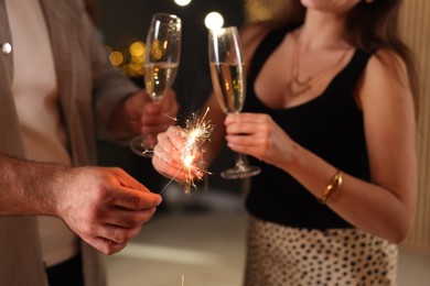 Photo of Friends celebrating New Year with sparklers and wine glasses indoors, closeup